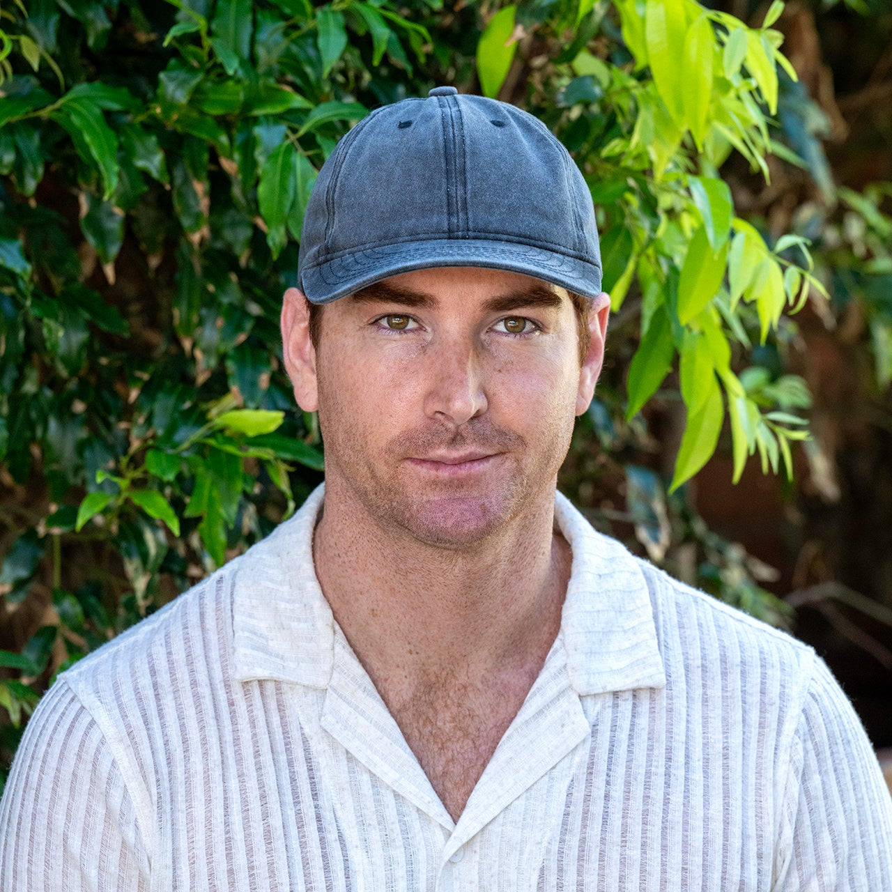 Man wearing a blue cap and white shirt against a green leafy background
