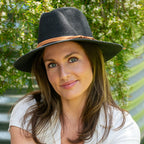 A woman wearing a black fedora with a tan band, standing outdoors.