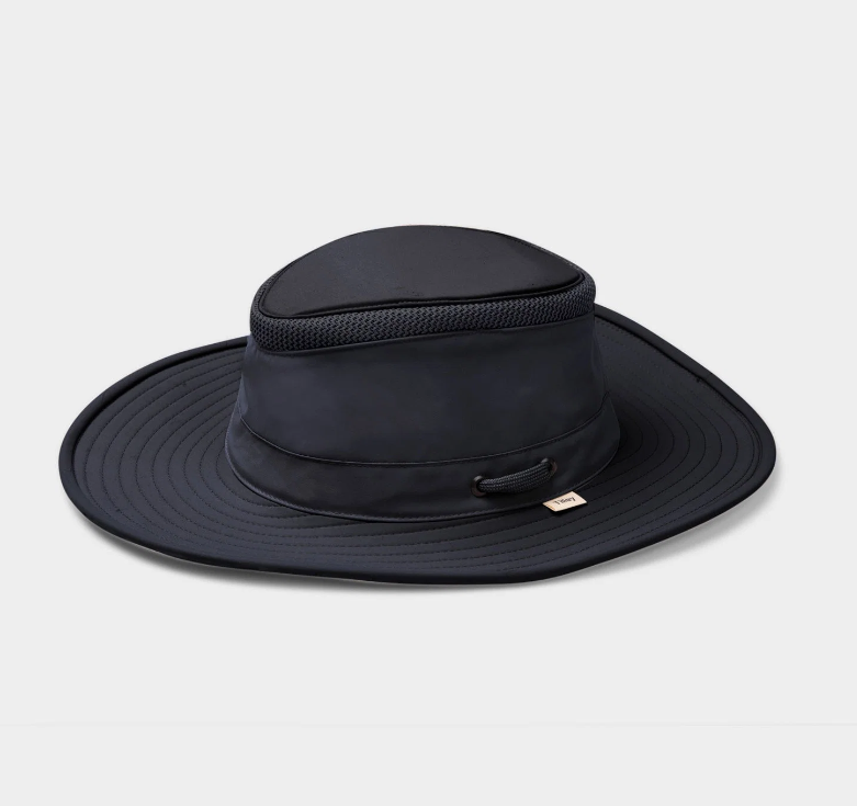 A navy wide-brim sun hat with a structured crown, mesh ventilation band, and a small gold brand tag on the side, photographed on a light gray background.