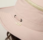 Close-up of a light mauve wide-brim sun hat with a woven beige band and a small beige brand tag reading Tilley.
