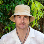 Man wearing a beige bucket hat and white shirt with green foliage in the background