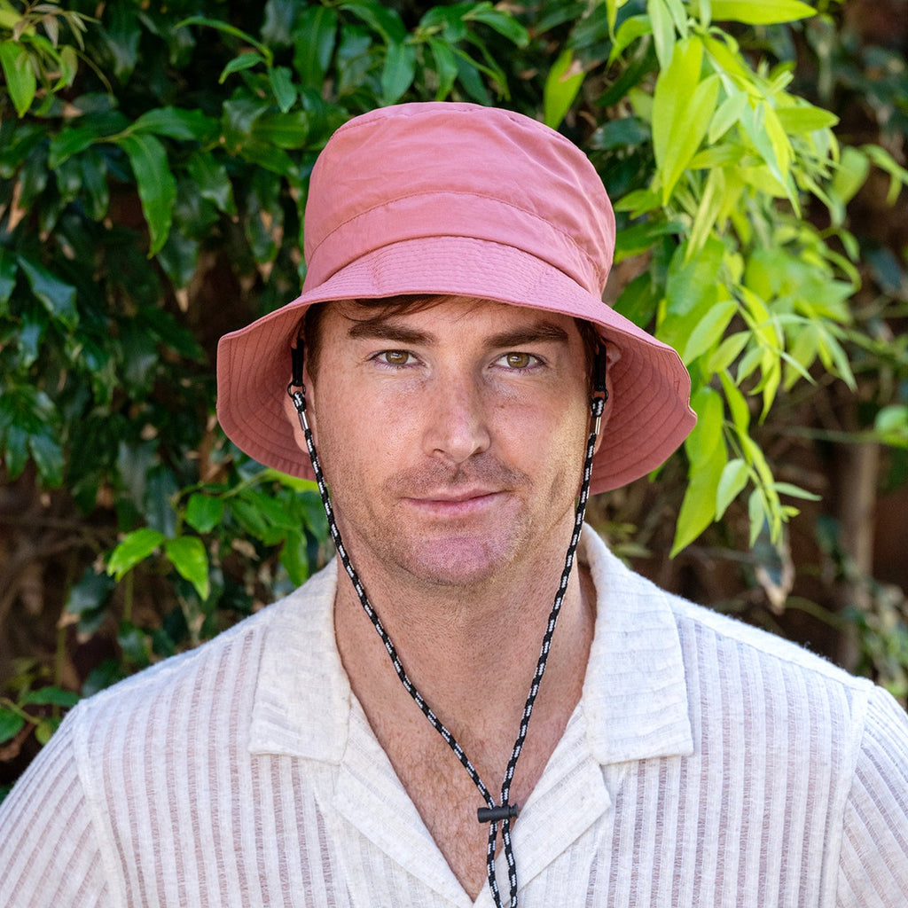 Man wearing a pink bucket hat and white shirt with green foliage in the background