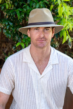 Man wearing a beige hat and white shirt against a green leafy background
