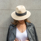 A woman wearing a beige wide-brimmed hat with a black trim, paired with a black leather jacket and blue jeans.